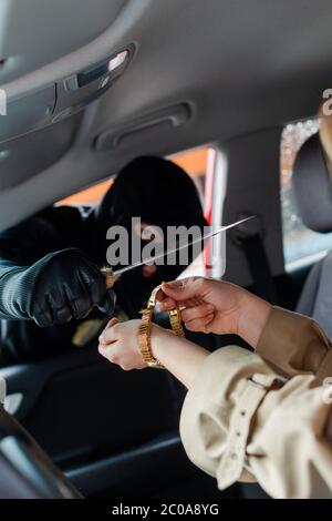 Selektiver Fokus des Diebes hält Messer in der Nähe der Frau, die Armbanduhr im Auto Stockfoto