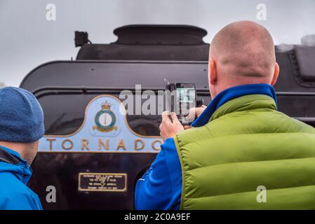 Rückansicht eines Eisenbahnenthusiasten, der mit dem Mobiltelefon Fotos von der britischen Dampflokomotive 60163 Tornado auf der Severn Valley Heritage Railway macht. Stockfoto