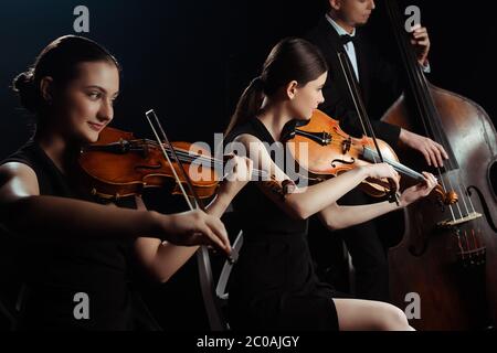 Trio von Musikern, die auf Kontrabass spielen und Violinen isoliert auf Schwarz Stockfoto