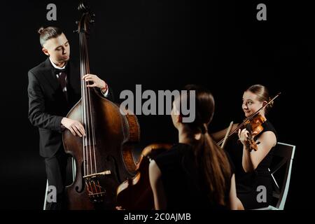 Trio von Musikern, die auf Kontrabass spielen und Violinen isoliert auf Schwarz Stockfoto