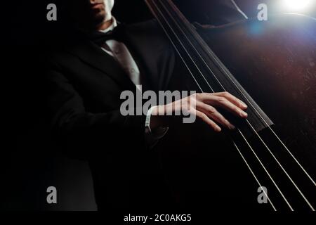 Kurzer Blick auf Musiker, der auf der dunklen Bühne auf Kontrabass spielt Stockfoto
