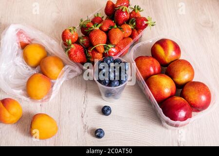 Fruchtkomposition mit Heidelbeeren, Erdbeeren, Nektarinen und Pfirsichen in Kunststoffbehältern auf Holzfläche Stockfoto