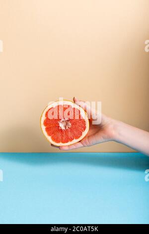 Cropped Ansicht der weiblichen Hand mit saftigen Grapefruit Hälfte auf beige und blau Hintergrund Stockfoto