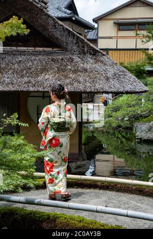 Japanischer junger Reisender, der in einem üppigen Garten in Kyoto traditionelle bunte Yukata (Sommerkimono) trägt. Stockfoto