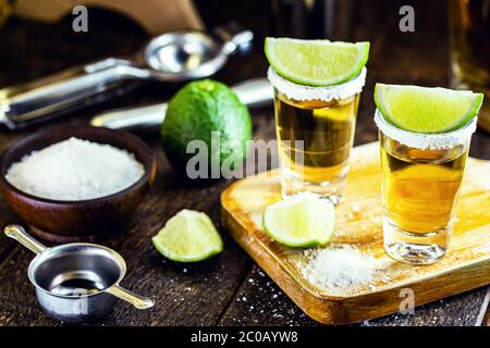 Mexikanischer Gold-Tequila mit Zitrone und Salz auf Holzgrund. Internationaler Tequila-Tag, Bar-Getränke-Einrichtung Stockfoto