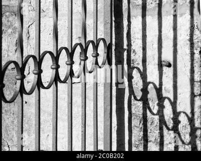 Detailansicht des dekorativen schmiedeeisernen Tores und des Schattens an der Wand. Schwarzweiß-Bild. Stockfoto