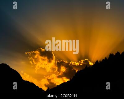 Sonnenstrahlen, die hinter der Wolke leuchten. Sonnenuntergang mit mountail Silhouetten. Stockfoto