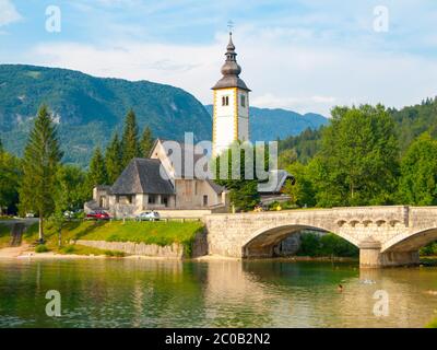 Kirche des Hl. Johannes des Täufers und alte Steinbrücke am Bohinjer See im Bergdorf Ribicev Laz, Julische Alpen, Slowenien. Stockfoto