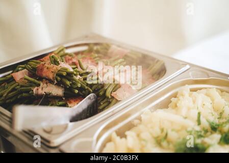 Quadratische Hotelpfanne aus Edelstahl mit Beilagen. Grüne Bohnen in Speckscheiben gerollt. Selbstbedienungsbuffet.Feier, Party, Geburtstag oder Hochzeit Stockfoto