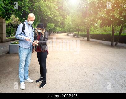 Ein grauhaariger Mann in einem Jeanshemd und mit Rucksack bittet das junge Mädchen um eine Wegbeschreibung. Sie schauen auf die Karte. Masken auf ihren Gesichtern. Das Mädchen Stockfoto