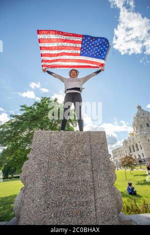 10. Juni 2020: Ein Aktivist hält eine Flagge hoch und steht dort, wo die Statue von Christoph Kolumbus wenige Minuten zuvor stand, bevor sie am 10. Juni 2020 in Saint Paul, Minnesota abgerissen wurde. (Bild: © Chris JuhnZUMA Wire) Stockfoto