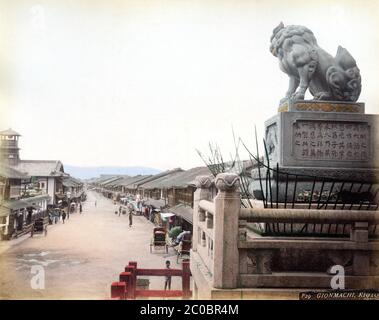 [ 1880er Japan - Gion, Kyoto ] - das Unterhaltungsviertel von Gion in Kyoto, wie von den Stufen des Yasaka Shrine gesehen. Die Straße ist mit einer Vielzahl von Teehäusern flankiert, wo die Kunden Essen, Tanz und Musik genießen konnten. Der Turm auf der linken Seite ist Teil der Yasaka Grundschule, die 1869 gegründet wurde (Meiji 2). Der Turm der Schule diente als Aussichtspunkt und zur Zeitmarke wurde alle zwei Stunden eine Trommel im Inneren des Aussichtspunkts erklang. Strommasten säumen die Straße noch nicht. Kyoto’s Elektrizitätsgesellschaft, Kyoto Dento Gaisha, nahm den Betrieb im Juli 1889 (Meiji 22) auf, so dass dieses Foto b aufgenommen wurde Stockfoto