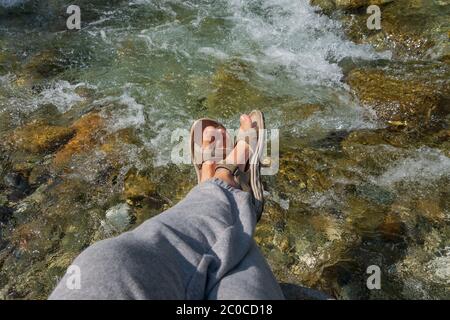 Frauen gebräunte Beine in offenen Sport-Sandalen auf einer Wanderung auf einem Bergfluss im Sommer. Reisekonzept, das Konzept Wandern Stockfoto