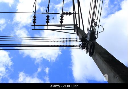 Teil der Kommunikationsleitungen und Stromleitungen auf elektrischen Pol gegen blauen Himmel und weißen Wolken als Vogel fliegenden Pass installiert, selektive Fokus Stockfoto