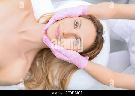 Closeup of beautician hands in gloves touching young woman's face. Plastic surgery concept. Facial beauty. Portrait of beautiful blonde female with pe Stockfoto