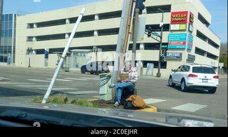 Obdachloser Mann bettelt am Rande des Parkplatzausgangs mit einer Wells Fargo Werbung hinter ihm. St. Paul Minnesota, USA Stockfoto