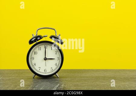 Schwarzer Retro-Wecker auf Holztisch und gelber Hintergrund. Stockfoto