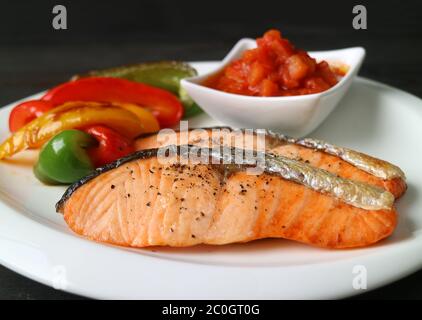 Hausgemachte Lachssteaks in der Pfanne mit gegrilltem buntem Gemüse und Salsa auf weißem Teller Stockfoto