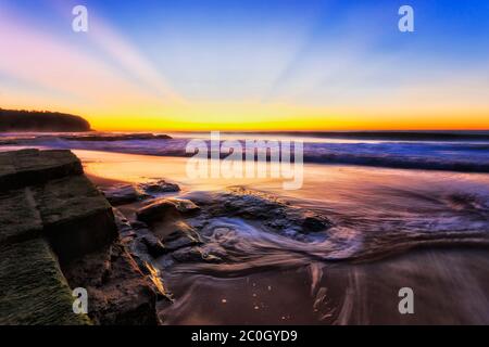 Dunkler Sonnenaufgang mit heller Sonnenkrone am Himmel über dem Pazifik Horizont in Seestraine vom Turimetta Strand von Sydney Northern Beaches. Stockfoto