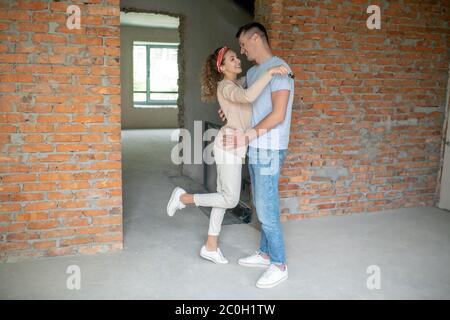 Junges Paar, das in dem leeren Raum mit Ziegelwänden steht und umarmt Stockfoto