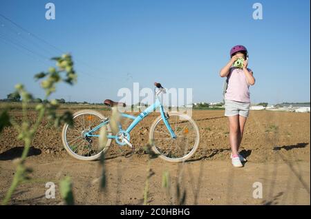 Nettes kleines Mädchen schießen auf dem Land mit ihrem Instant-Bild Fotokamera. Sie hat ein schönes Retro-Fahrrad an der Seite geparkt Stockfoto