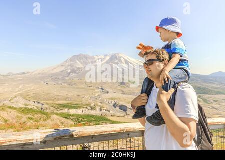 Junger Vater trägt auf Schultern sein kleiner Sohn, der mit Spielzeugchippmunk auf einer Spur mit Mount St. Helens im Hintergrund spielt Stockfoto