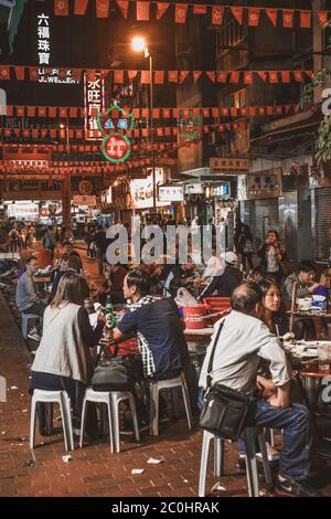Menschen sitzen und essen Street Food auf dem Abend Temple Street Market in Hong Kong Stockfoto