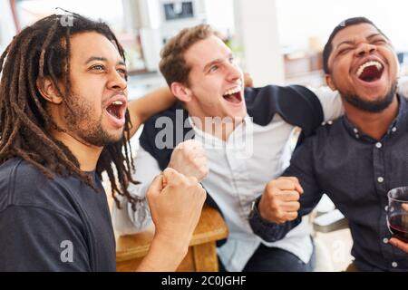 Freundliche Männer jubeln zusammen, während sie Fußball zu Hause beobachten Stockfoto