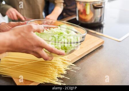 Hände bereiten Salat und Mittagessen in der Küche mit Schüssel und Spaghetti Stockfoto