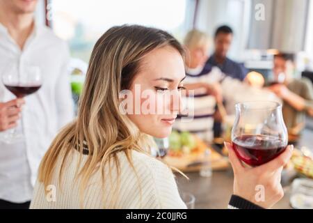 Junge Frau mit einem Glas Rotwein vor einer Gruppe von Freunden in der Gemeinschaftsküche Stockfoto