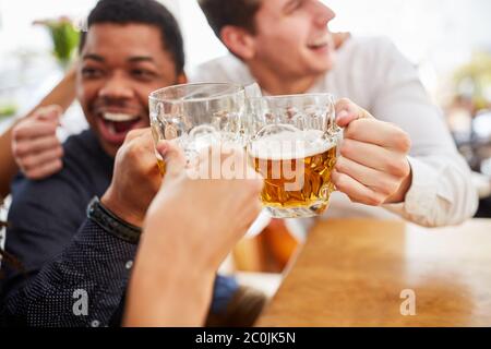 Lachend jubelnde Männer trinken Bier und toasten sich im Biergarten auf dem Oktoberfest Stockfoto