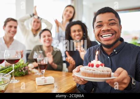 Afrikanischer Mann hält Kuchen mit Kerze an seinem Geburtstag auf seiner Geburtstagsfeier Stockfoto