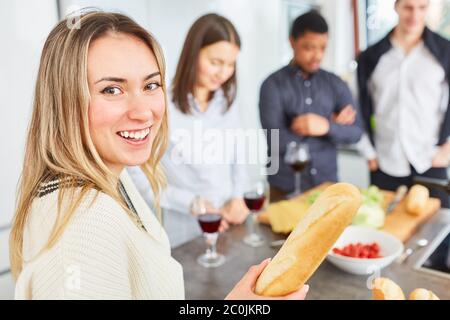 Glückliche Frau mit Baguette, die zusammen mit Freunden in der Gemeinschaftsküche Essen zubereitet Stockfoto