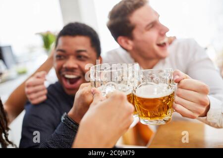 Lachend jubelnde Männer trinken Bier und stoßen sich an, während sie Fußball schauen Stockfoto