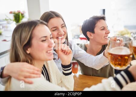 Glückliche Frauen umarmen sich gegenseitig, während sie Fußball und klirrende Gläser Bier beobachten Stockfoto