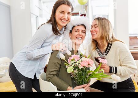 Lachende Freundinnen feiern mit Braut auf der Junggesellinnenparty mit Blumen und Wein Stockfoto