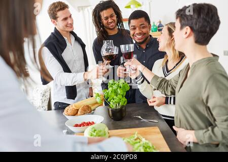 Glückliche Gruppe von Freunden stoßen mit einem Glas Wein in der Küche an, bevor sie zusammen essen Stockfoto