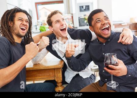Eine Gruppe von Männern als Freunde jubeln zusammen, während sie Fußball oder Sport zu Hause beobachten Stockfoto