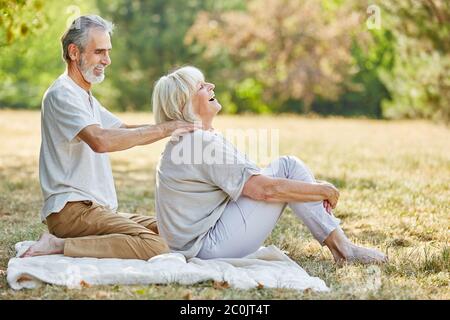 Der alte Mann massiert im Sommer im Garten den Hals seiner Frau Stockfoto