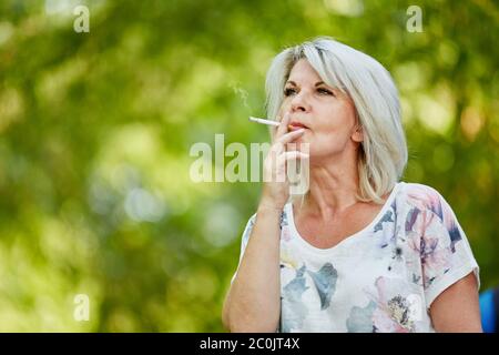 Alte Frau raucht eine Zigarette in der Natur Stockfoto
