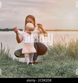 Ein Mädchen lernt mit ihrer Mutter in die Natur zu gehen. Mutter und Tochter, Lernen und Entwicklung. Die ersten Schritte des Kindes. Glückliche Momente des Lebens. Stockfoto