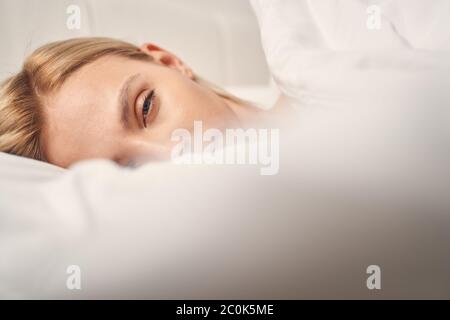 Schläfrige blonde Frau im Bett, die nach vorne schaut Stockfoto