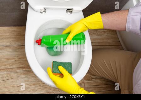 Mann, der den Toilettensitz desinfiziert, indem er ein grünes Desinfektionsmittel aus einer Flasche sprüht. Ein Mann desinfiziert zu Hause eine Toilette. Stockfoto