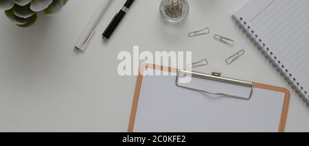 Von oben Blick auf den weißen Schreibtisch mit Papier auf der Zwischenablage, Schreibwaren, Terminkalender und andere Büromaterialien Stockfoto