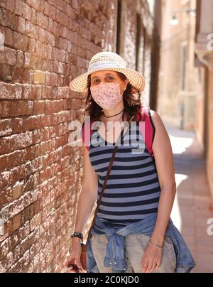 Frau mit Strohhut und OP-Maske während der Corona Virus Pandemie beim Besuch der Insel Venedig in Italien Stockfoto