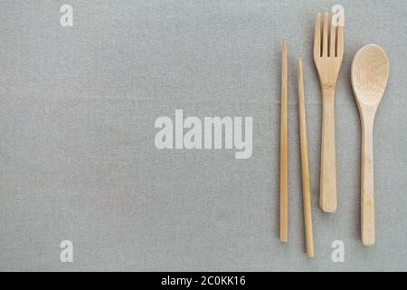 Wiederverwendbares und umweltfreundliches Utensil, einschließlich Bambuslöffel, Gabel und Essstäbchen auf der Seite von beigem oder grauem Hintergrund. Speicherplatz kopieren. Stockfoto