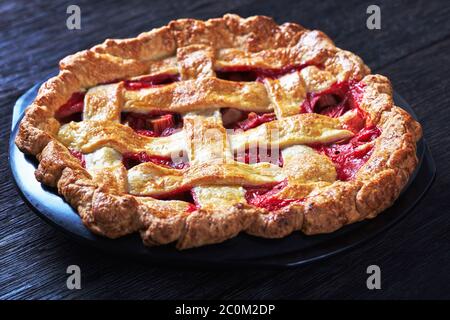 Hausgemachte ganze Erdbeer Rhabarb Pie mit Gitter auf einem dunklen Holztisch dekoriert, Landschaftsansicht von oben, Nahaufnahme Stockfoto