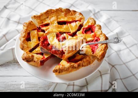 Frisch gebackene hausgemachte Erdbeer Rhabarb Pie Scheiben auf einem weißen Kuchen Platte auf einem Holztisch, Blick auf die Landschaft Stockfoto