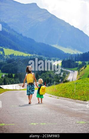 Kleine Kinder, Junge Brüder mit Rucksäcken und Koffer, reisen auf der Straße zu malerischen Bergen Stockfoto