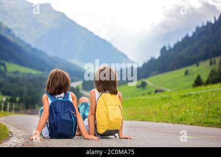 Kleine Kinder, Junge Brüder mit Rucksäcken und Koffer, reisen auf der Straße zu malerischen Bergen Stockfoto